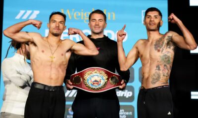 Two light welterweight fighters flex on the scale during an official weigh-in as an official stands between them holding a championship belt.