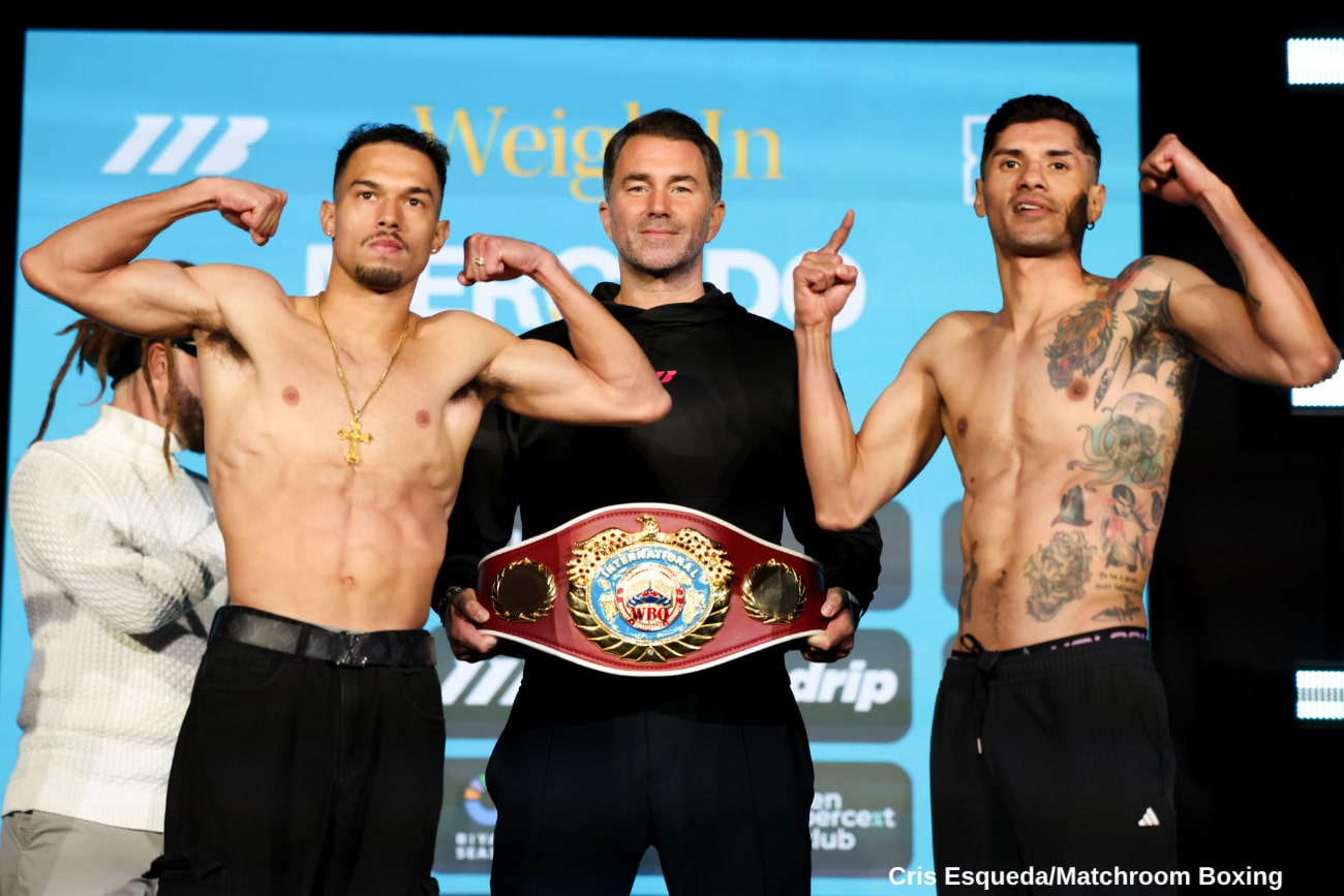 Two light welterweight fighters flex on the scale during an official weigh-in as an official stands between them holding a championship belt.