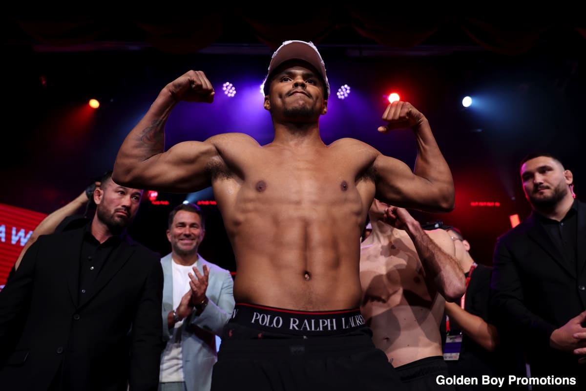 A shirtless Shakur Stevenson flexes both arms on stage during the official weigh-in for his fight against William Zepeda on July 11, 2025, with team members and officials watching behind him.