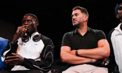 Richardson Hitchins speaks into a microphone during a press event while promoter Eddie Hearn sits beside him with folded arms, listening.