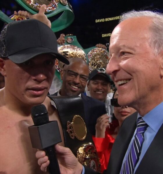 David Benavidez celebrates a dominant victory over Gilberto Ramirez at T-Mobile Arena, holding multiple WBC belts while giving a post-fight interview, with his team cheering in the background.
