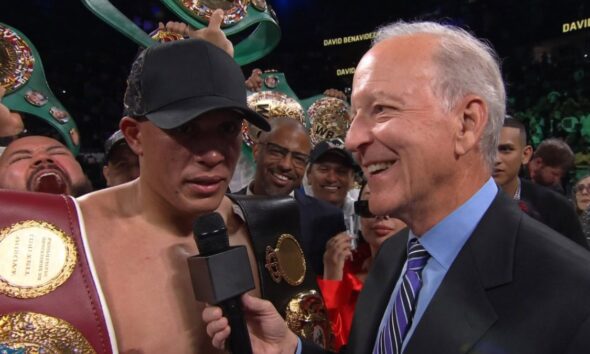 David Benavidez celebrates a dominant victory over Gilberto Ramirez at T-Mobile Arena, holding multiple WBC belts while giving a post-fight interview, with his team cheering in the background.