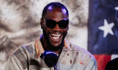 Deontay Wilder smiles during a media appearance with a United States flag behind him