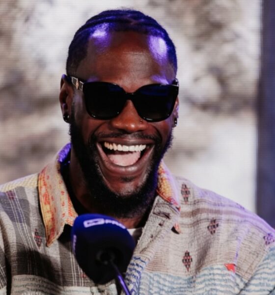 Deontay Wilder smiles during a media appearance with a United States flag behind him
