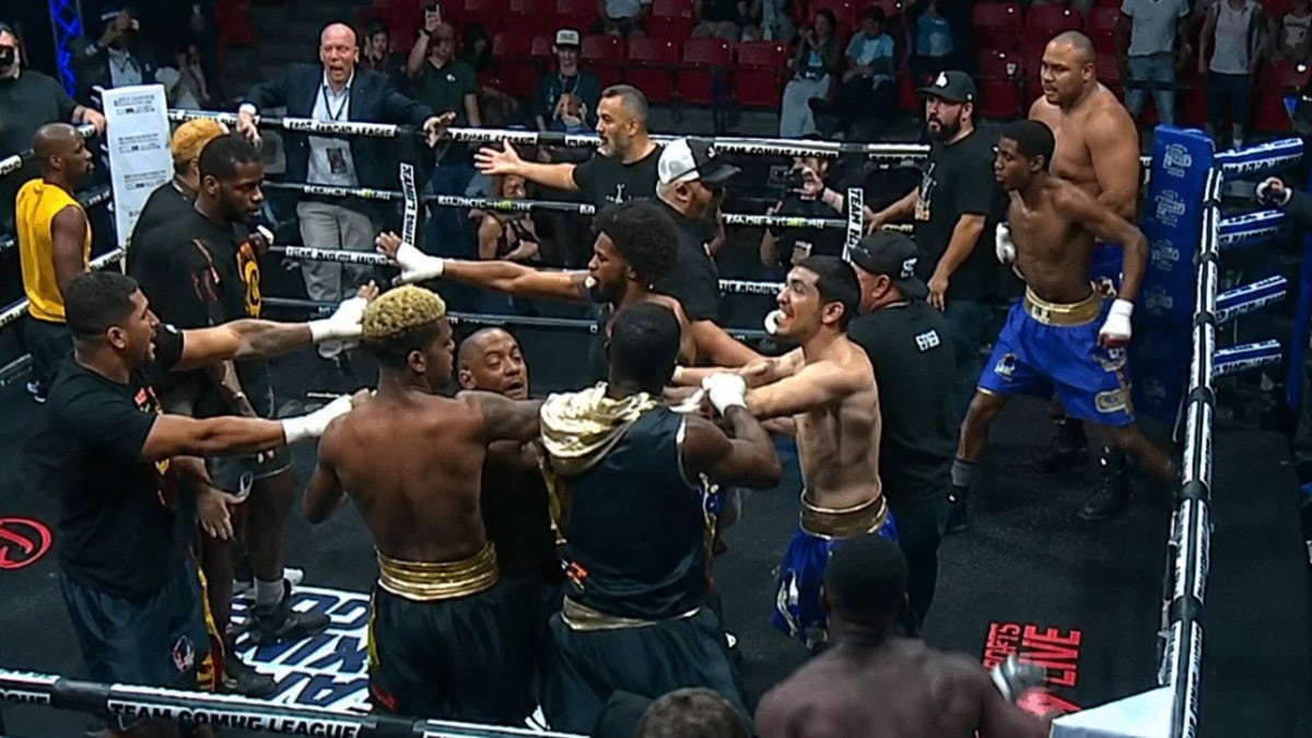 Multiple boxers and team members confront each other inside the ring during a Team Boxing League event as officials attempt to separate them in the chaos